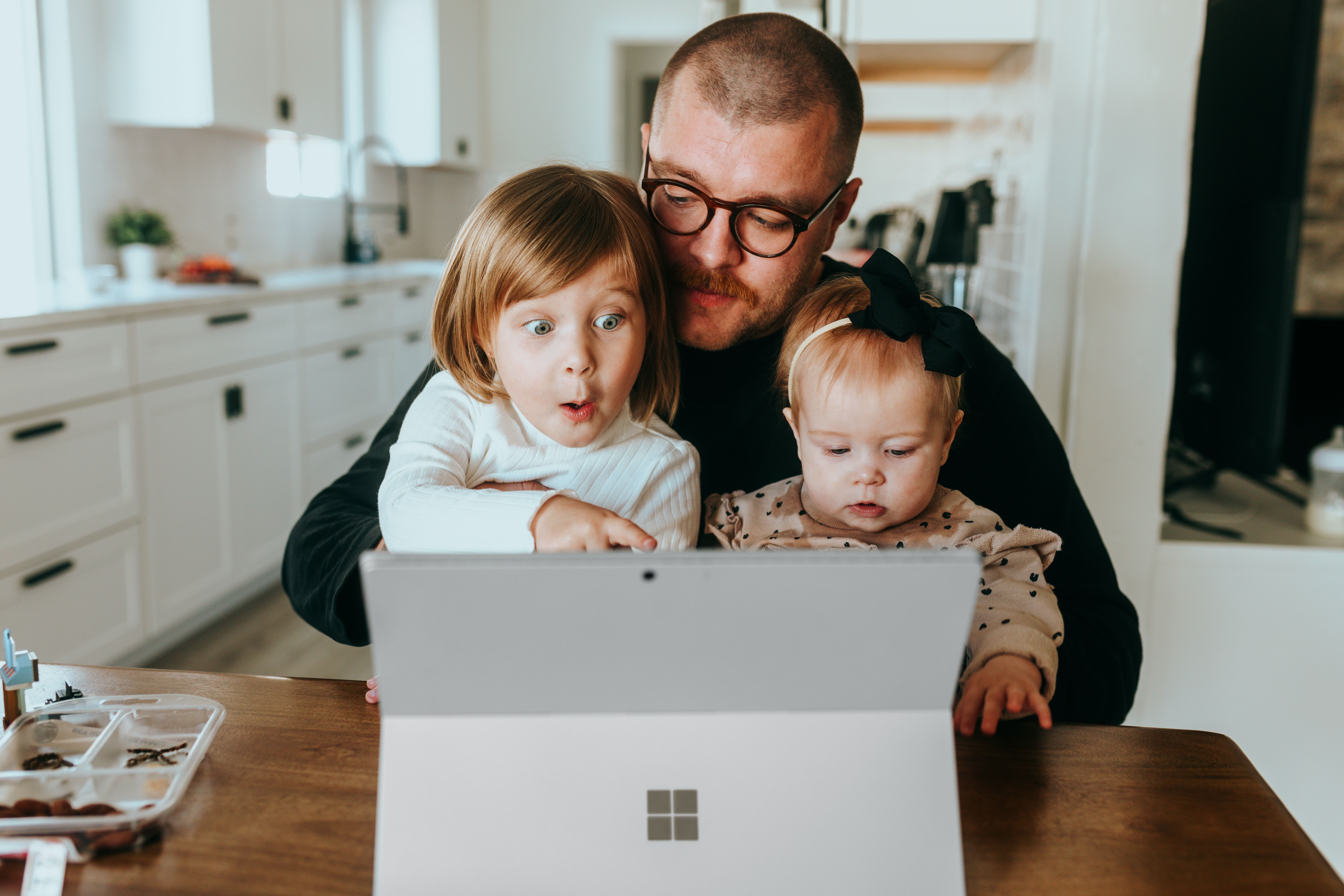 A man holding two children and looking at a laptop