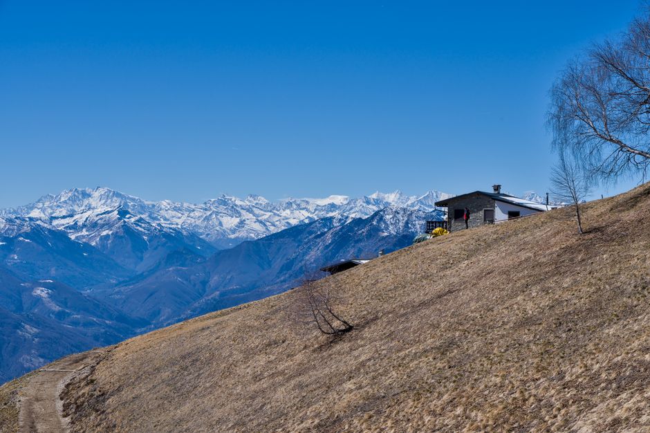 Cozy cabin overlooking breathtaking snow-capped Alps under a clear blue sky.