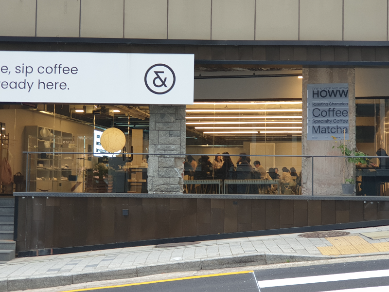 카페 안쪽 사람들이 가득차있다. 기둥에 HOWW라는 글씨가 보인다.