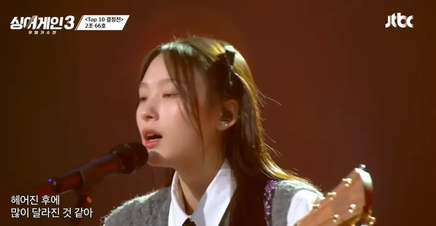 싱어게인3- 흰셔츠&amp;#44; 회색 조끼를 입고 검은색 넥타이를 맨체 갈색기타를 치며 긴생머리 양쪽으로 삔을 꽂은채 스탠딩마이크 앞에서 노래하는 66호