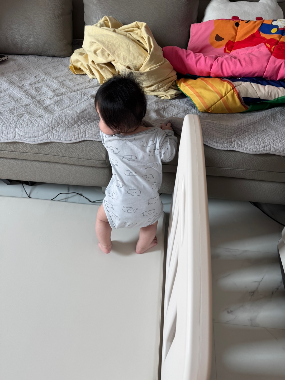 소파에 기대어 서있는 아기