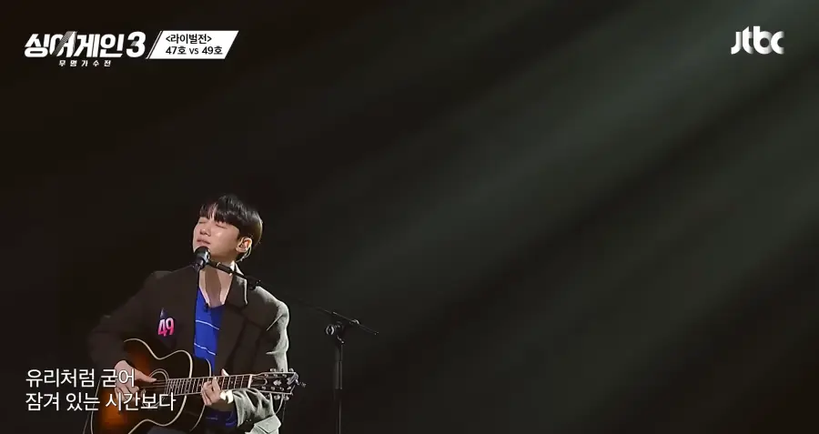 싱어게인3 - 검은색 자켓에 파란 가로줄무늬 티를 입고 갈색기타를 치며 스탠딩 마이크앞에서 눈감고 노래부르는 49호