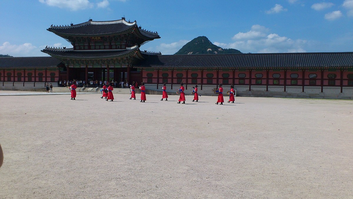 Royal guards in red Joseon-era robes marching across the square in front of Heungnyemun Gate during the changing of the guard at Gyeongbokgung Palace