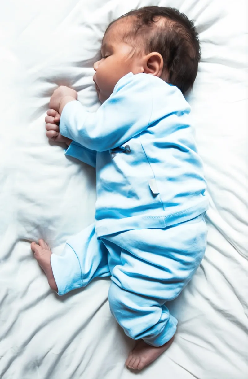 하늘색 잠옷을 입고 침대 위에서 잠든 아기의 모습