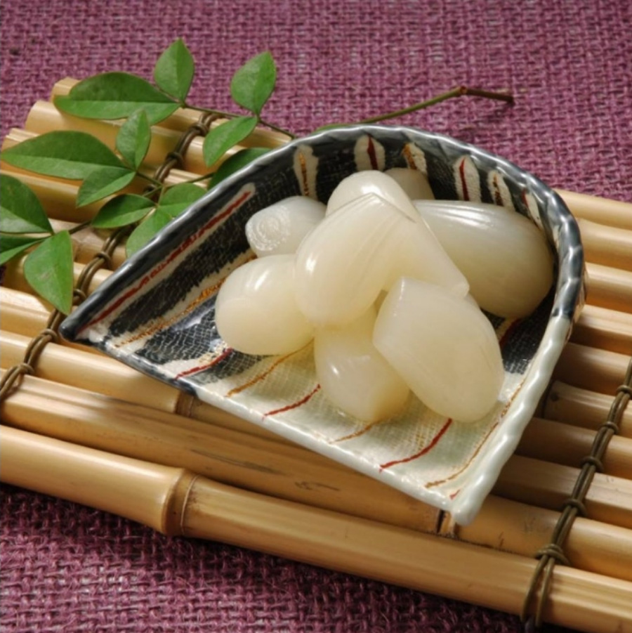 보라색 바닥 위에 대나무로 만든 깔판을 놓아두고 그 위에 키 모양의 유리 그릇에 식초에 절인 염교를 여러 개 놓아두고 찍은 사진