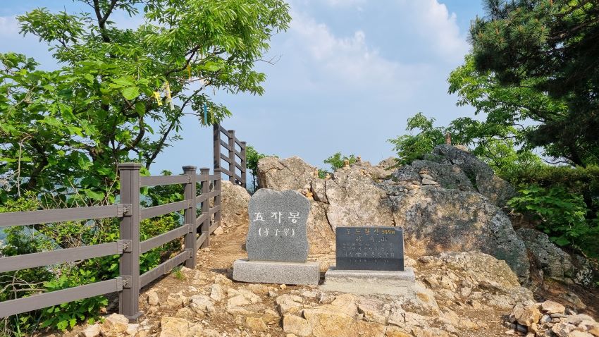 정상에 정상석, 효자봉으로 새겨져 있음, 뒤로는 안전 난간, 푸른하늘,