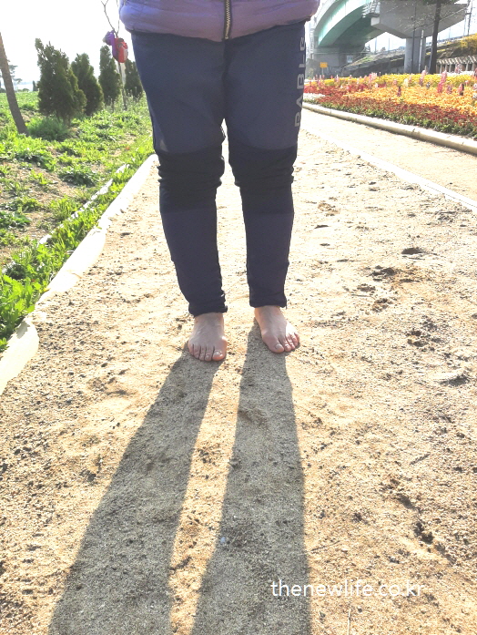 A woman walking barefoot on a soft soil trail at Guri Hangang Citizens Park, enjoying the quiet morning air.-구리 한강시민공원 부드러운 흙길 위를 맨발로 걷는 여성 – 아침 공기와 자연의 감촉을 함께 느끼는 순간