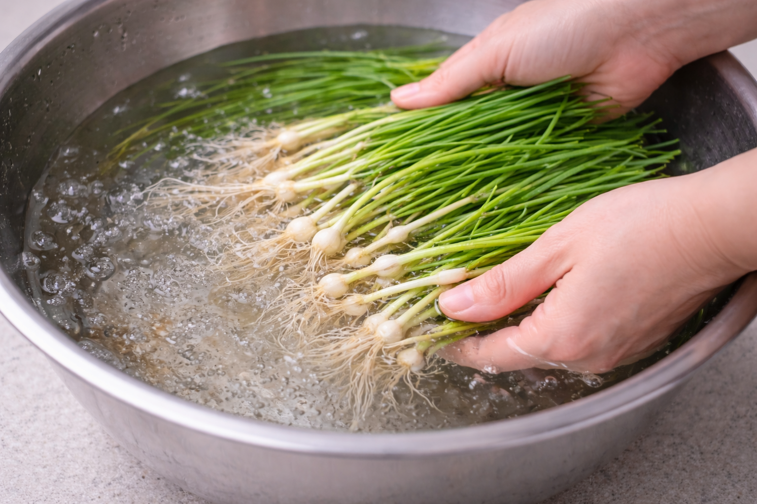 큰 볼에 담긴 달래를 물에서 살살 흔들어 흙을 가라앉히며 세척하는 모습입니다.