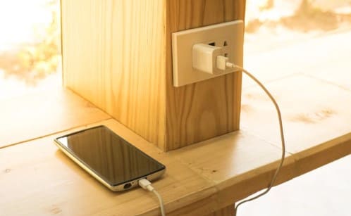 나무 선반위에 휴대폰이 있고 충전기가 연결되어 있다.