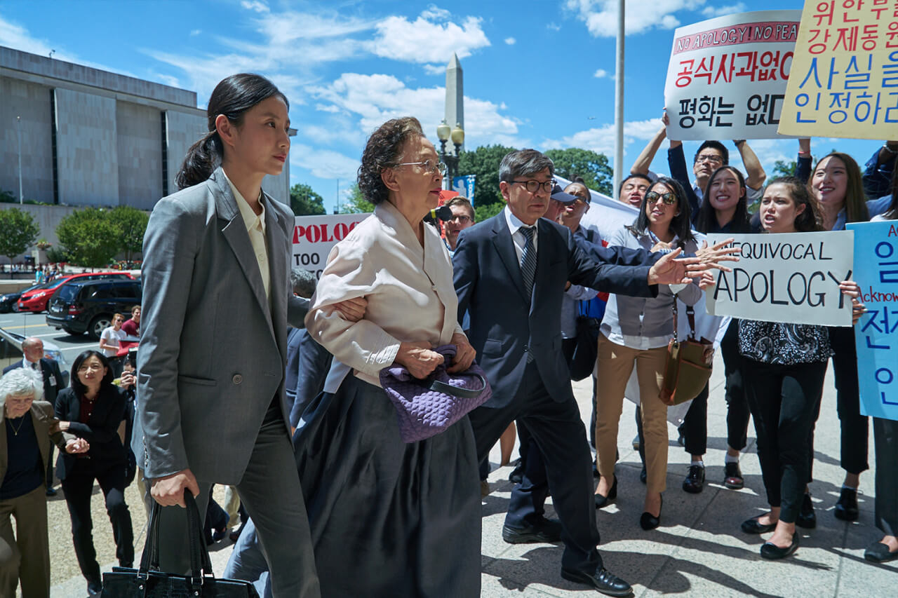피켓을 들고 있는 사람들 사이를 걸어 들어가는 옥분