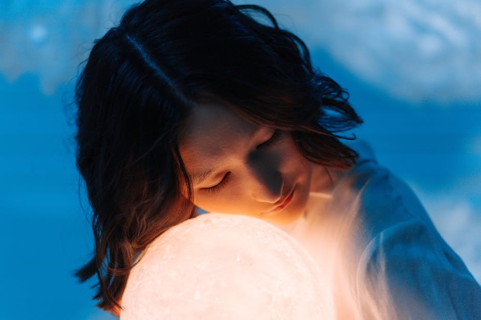 A serene portrait of a woman embracing a glowing orb, set against a soft blue background.