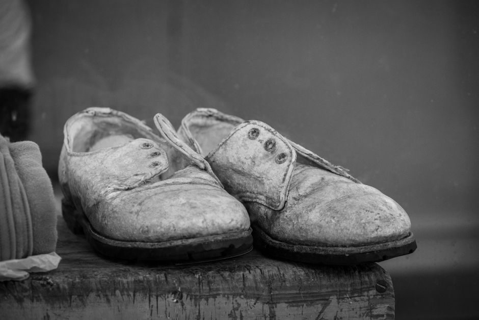 Black and white photograph of vintage worn leather shoes resting on a wooden surface, showcasing age and history.