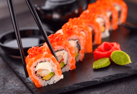 네모난 검정 접시에 연어초밥 8개가 있다. 검정 젓가락으로 초밥 한개를 집고 있다.