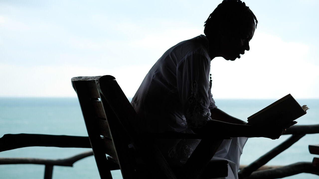 푸른 바다, 하늘을 배경으로 한 사람이 의자에 앉아서 책을 읽고 있다.