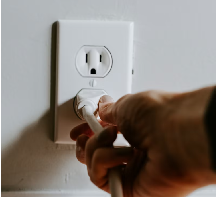 벽면 콘센트에서 전기 플러그를 손으로 뽑는 모습