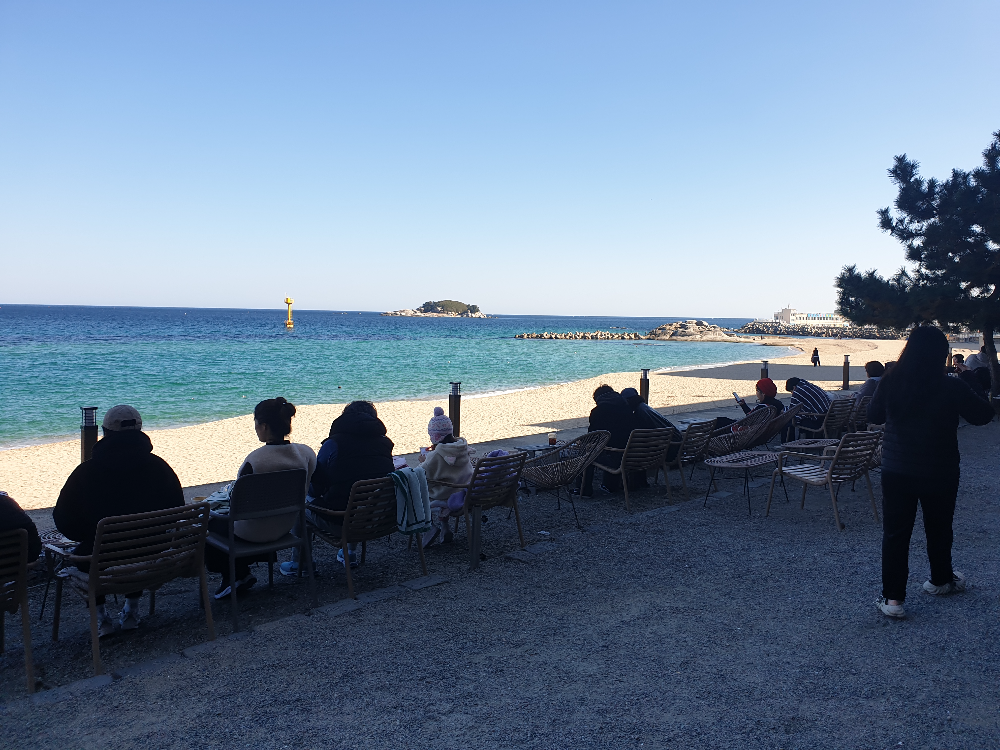 바다가 보이는 야외 테이블에 사람들이 앉아 있다.