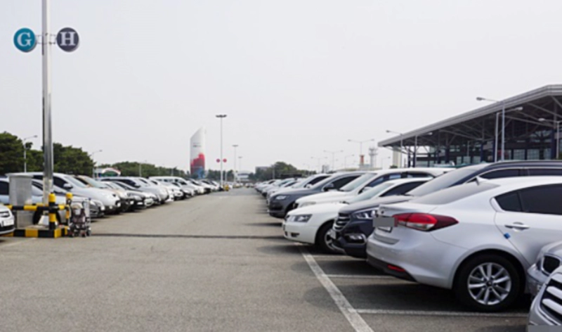 회색 아스팔트 주차장 양 옆에 차가 줄지어 주차됨