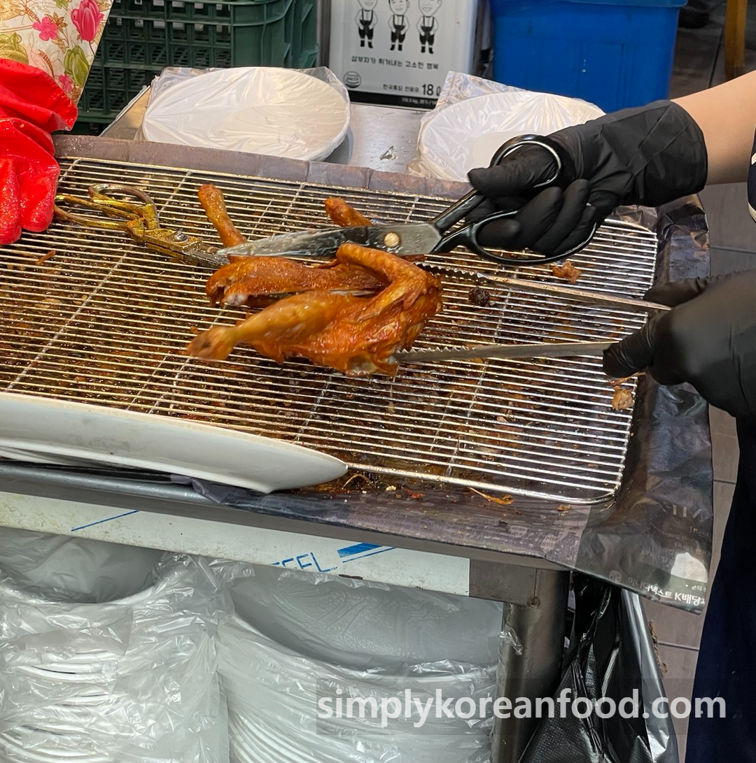 A freshly fried whole chicken being cut into pieces with kitchen scissors and tongs at Korea Tongdak in Dongmyo.