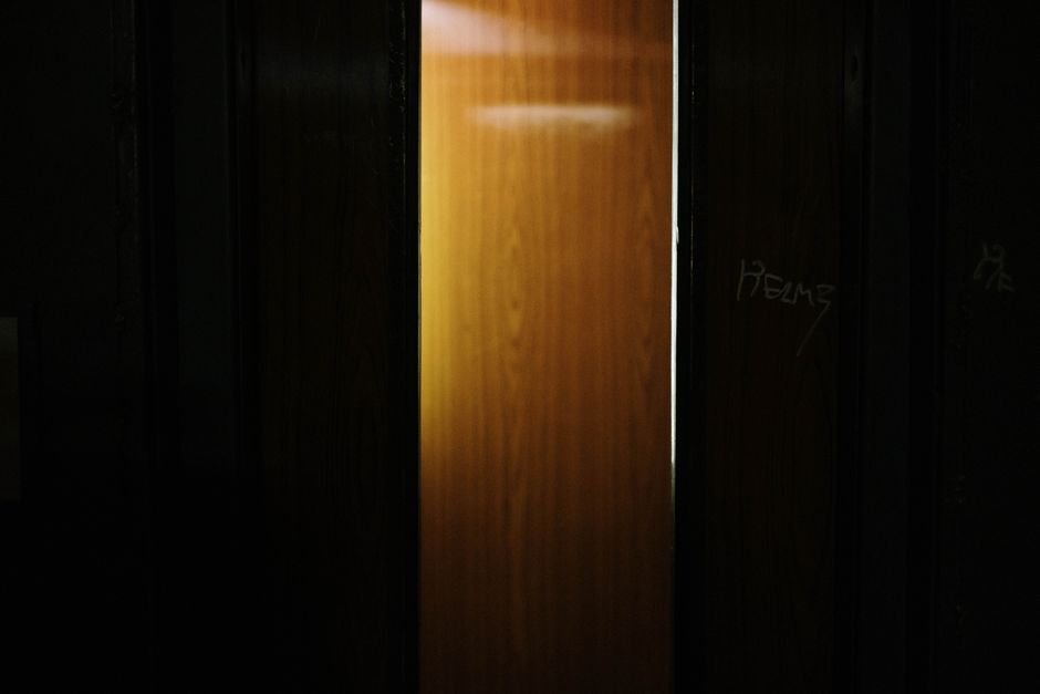 A partially open wooden door revealing light shining through a dark interior.
