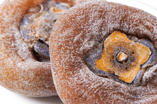 납작한 곶감 2개가 나란히 있다. 표면에는 하얀 시설이 가득하고 꼭지는 주황색이다.