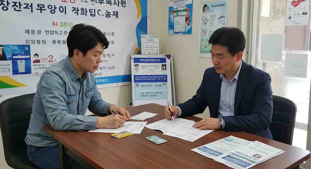 행정복지센터에서 에너지바우처 상담을 받는 소상공인 남성. 공무원과 대면 상담 중 서류 작성을 하고 있는 장면
