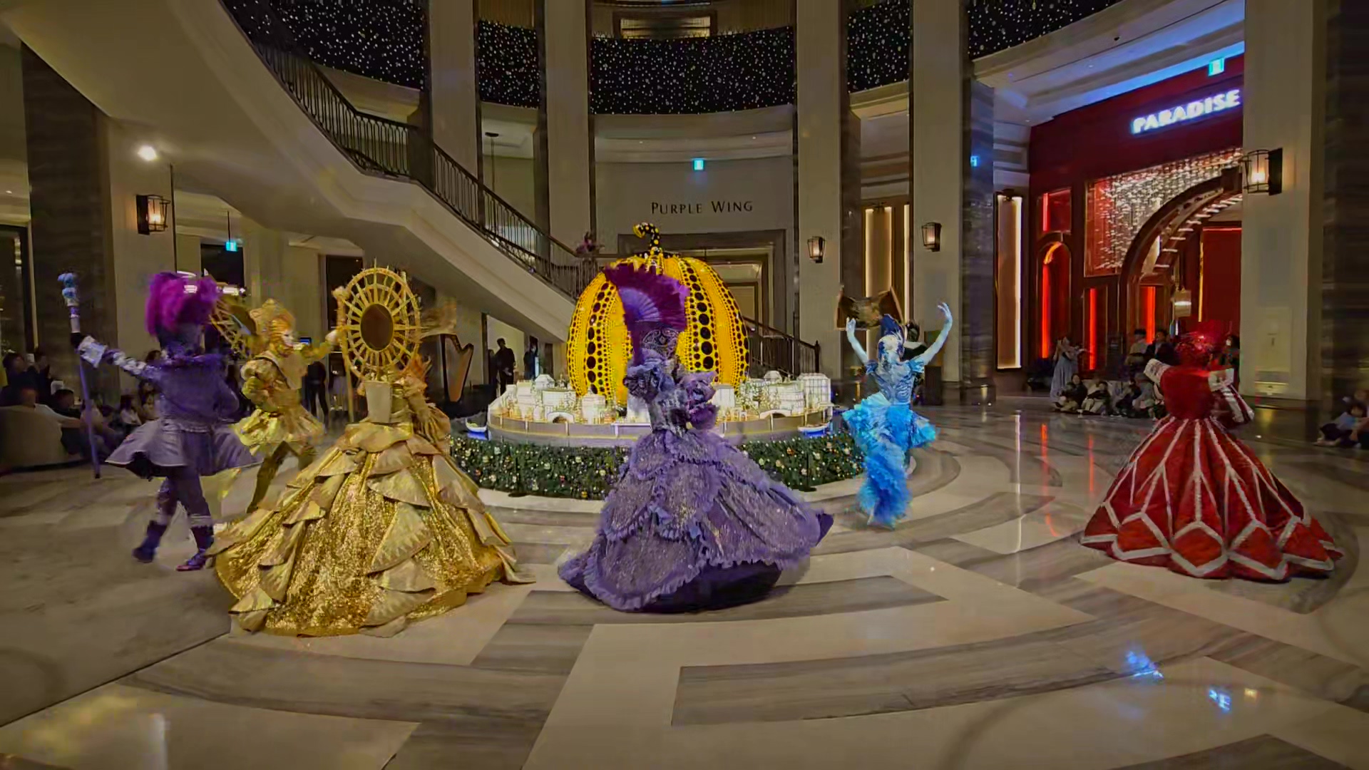 파라다이스 시티 크리스마스 시즌 공연 LUNA ECLIPSE 장면. 퍼포머들이 색색의 무도회 의상을 입고 원형 무대 주변에서 춤추고 있는 모습