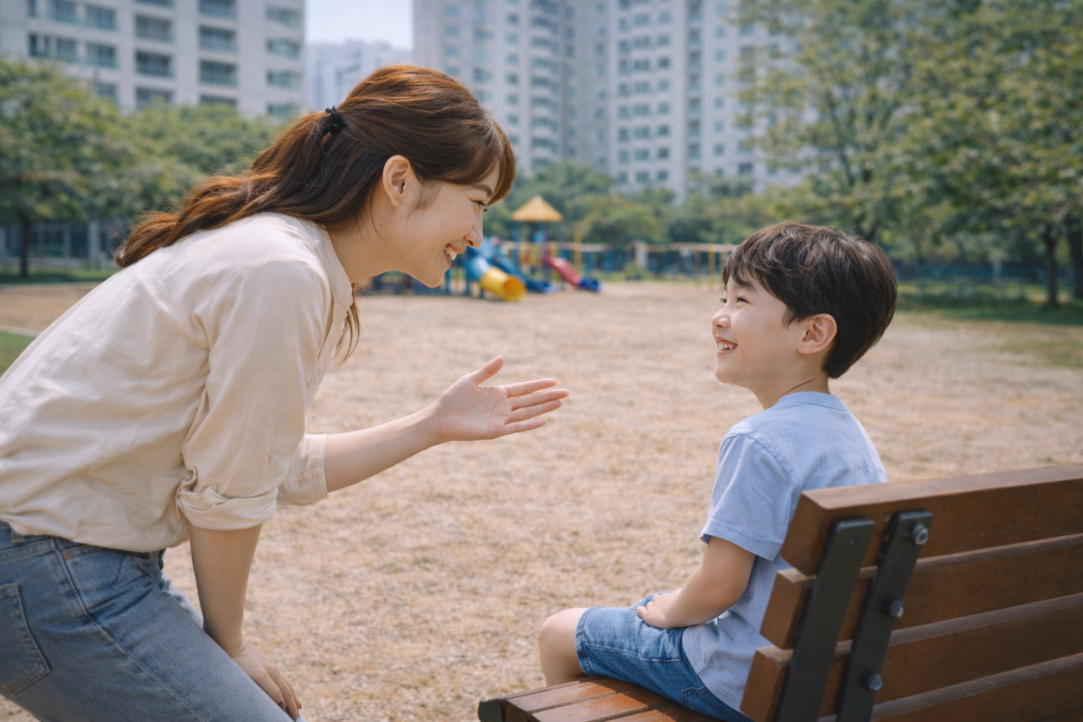 놀이터 벤치에 앉은 아이에게 엄마가 허리를 숙여 손짓과 함께 다정하게 이야기하고 있는 모습