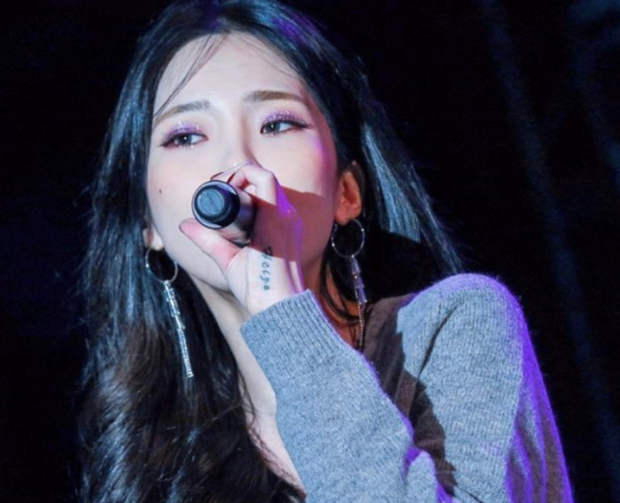 가수-헤이즈가-무대에서-마이크를-들고-노래를-하고-있는-사진으로-마이크를-든-왼손날에-타투가-있다.