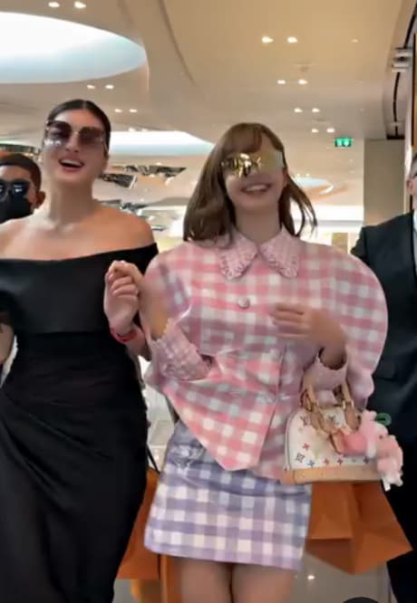 쇼핑몰에서 선글라스를 착용한 블랙핑크 리사가 핑크 체크 코트와 미니 스커트 차림으로 라부부 키링이 달린 명품 가방을 들고 환하게 웃으며 걷고 있는 장면