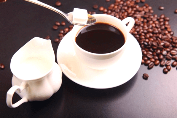 하얀 커피잔에 블랙커피가 있다. 스푼으로 하얀 각설탕을 넣으려고 한다. 주변엔 고동색 커피콩들이 깔렸다.