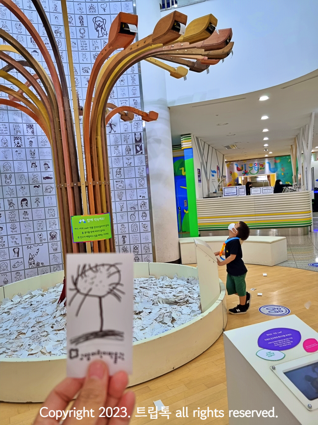 금속으로 된 기둥에서 그림이 떨어지는걸 쳐다보는 아이와 그 아이가 그린 그림