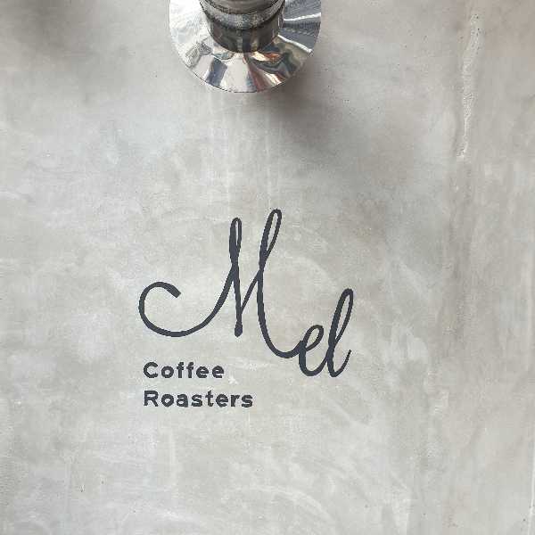회색 벽에 영어로 멜 커피 로스터스라고 쓰인 로고가 프린트 되어 있다.