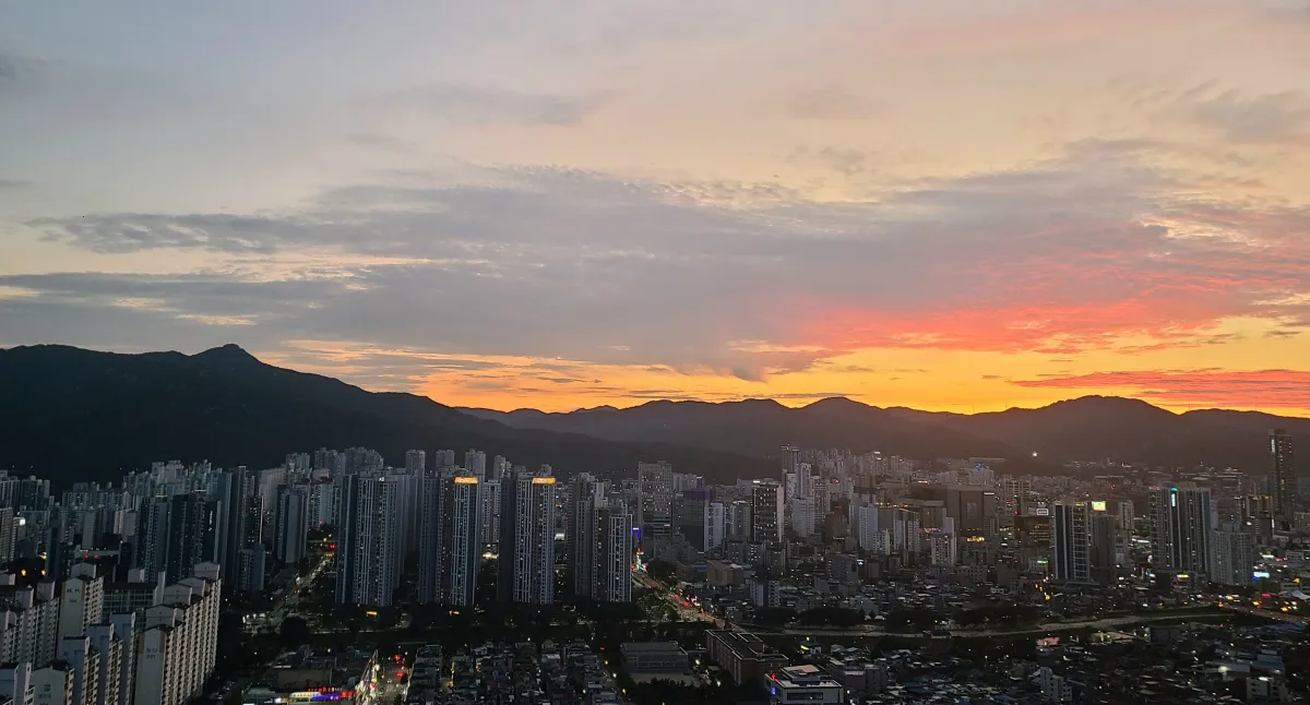 석양이지는하늘-불빛이켜진-아파트건물뒤로-길게이어진-산등성이