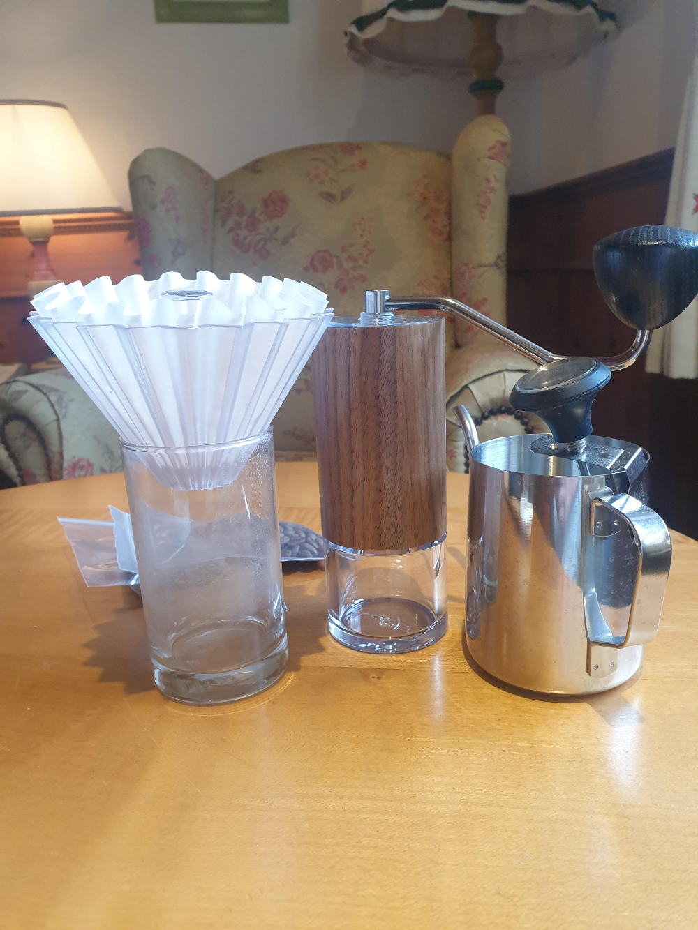 우드 테이블 위에 컵과 그라인더 그리고 드립포트가 올려져 있다.