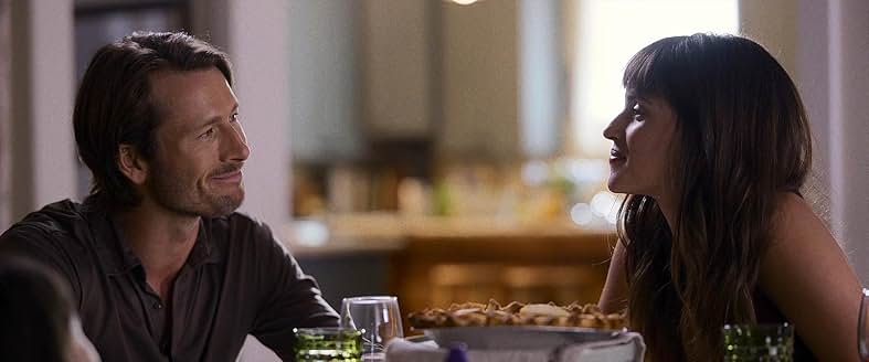 영화 Hit Man에서 두 주인공이 저녁 식사 자리에서 미소 지으며 대화하는 장면