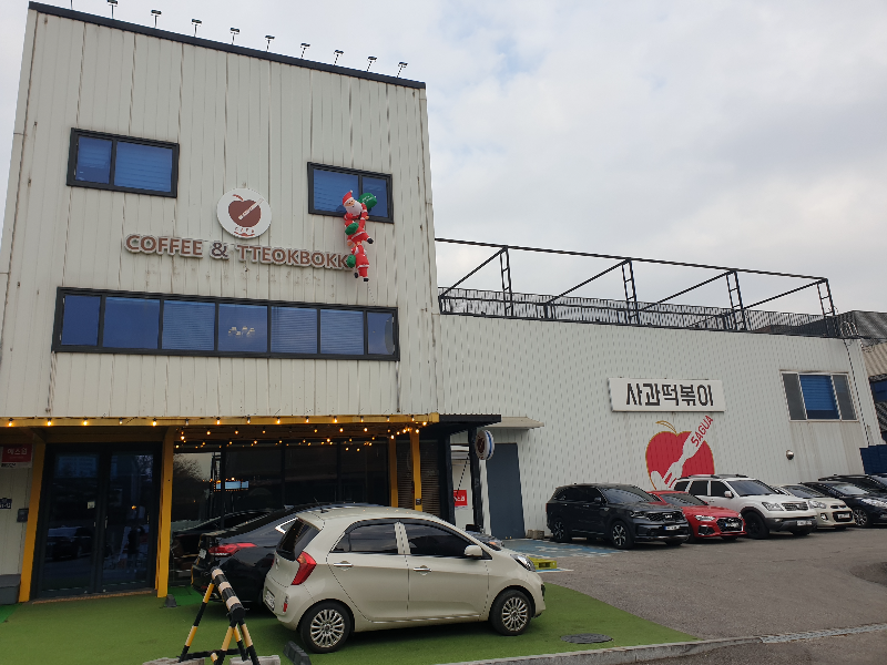공장 건물과 같은 사과떡볶이 카페 외관. 카페 전면과 왼쪽 전용 주차 공간이 있다.