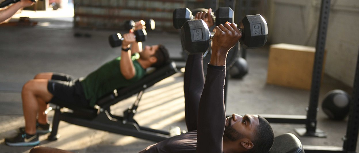 실내 헬스장에서 근력 운동을 하고 있는 두 남성의 모습