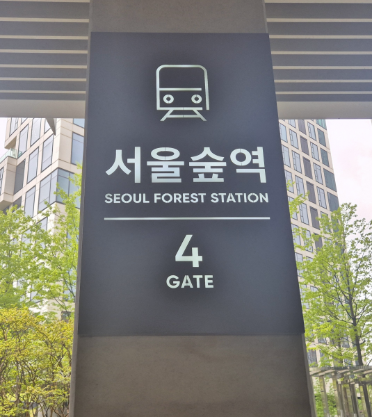 서울숲역 4번 게이트 출구 표시판, 뒤로 푸른 나무와 현대적인 건물이 보임