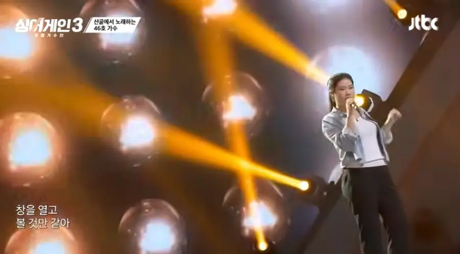 싱어게인3-
회색 배경 무대위 청색 셔츠에 흰티를 받쳐입고 검은마이크를 오른손으로 들고 긴머리를 뒤쪽 하나로 묶고 노래하는 46호가 정면을 바라보는 모습