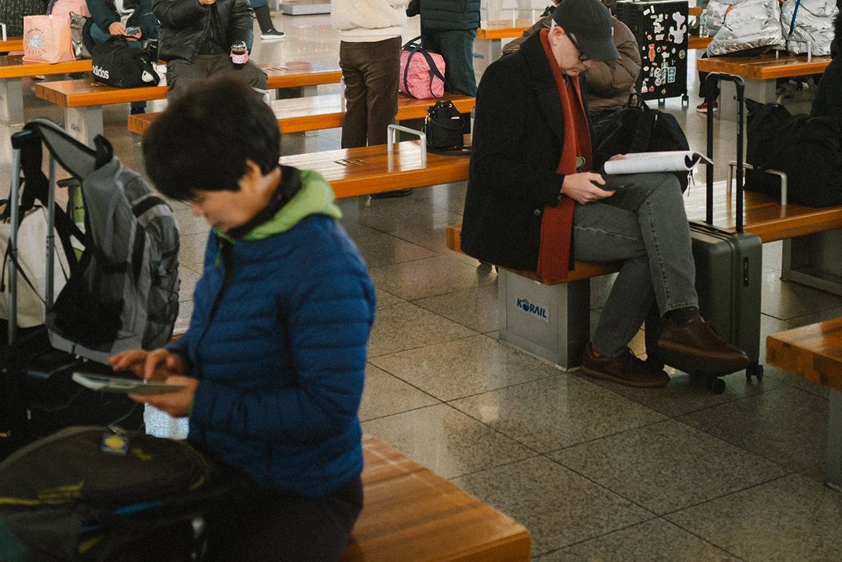한 의자에는 남자가 앉아있고 다른 한 의자에는 여자가 앉아있다. 둘은 대각선에 위치하고 있으며 한 명은 책을 다른 한 명을 휴대폰을 보고 있어 대비가 명확하다