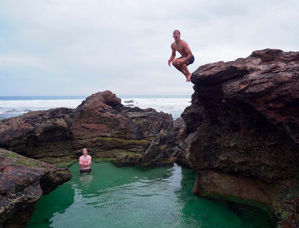 바다에 있는 바위덩어리 위에서 남자가 점프를 하고있다