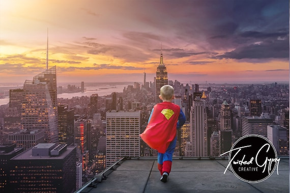 어린 소년이 도시 빌딩 위에서 슈퍼맨 복장을 하고 도시를 전망하는 모습