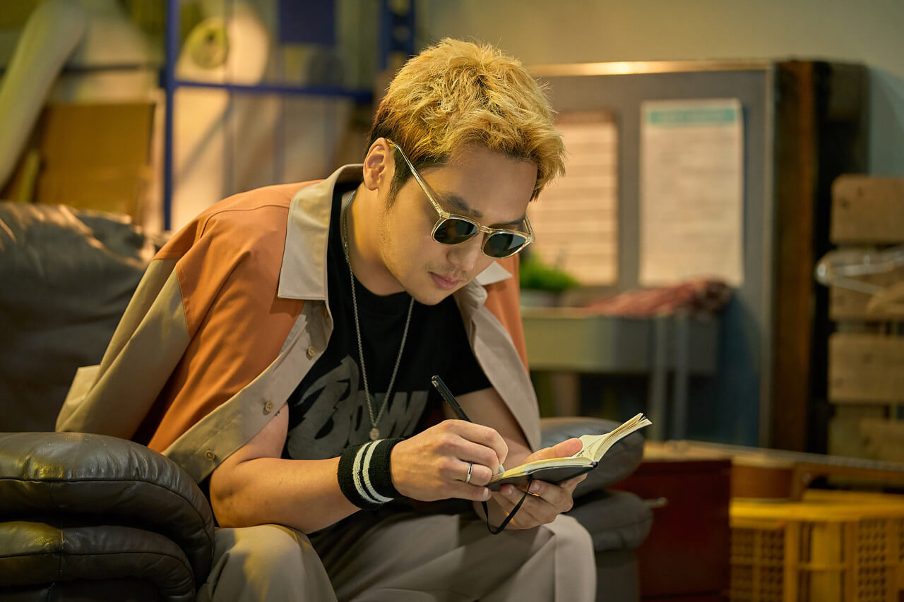 선글라스를 낀 채 쇼파에 앉아 메모하는 요한