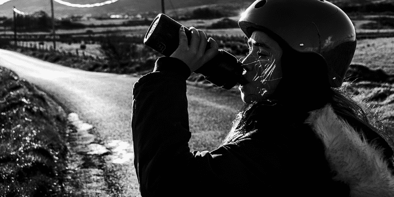 바이크 헬멧을 쓴 여자가 물을 마시고 있다