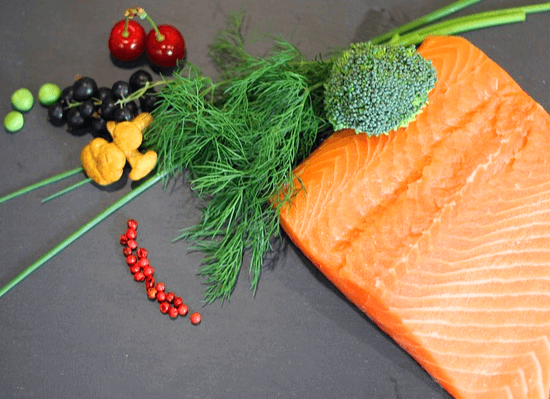 회색 식탁 위에 네모난 주황색 연어가 있고, 주변엔 빨간 체리, 완두콩 3개, 파슬리가 있다.