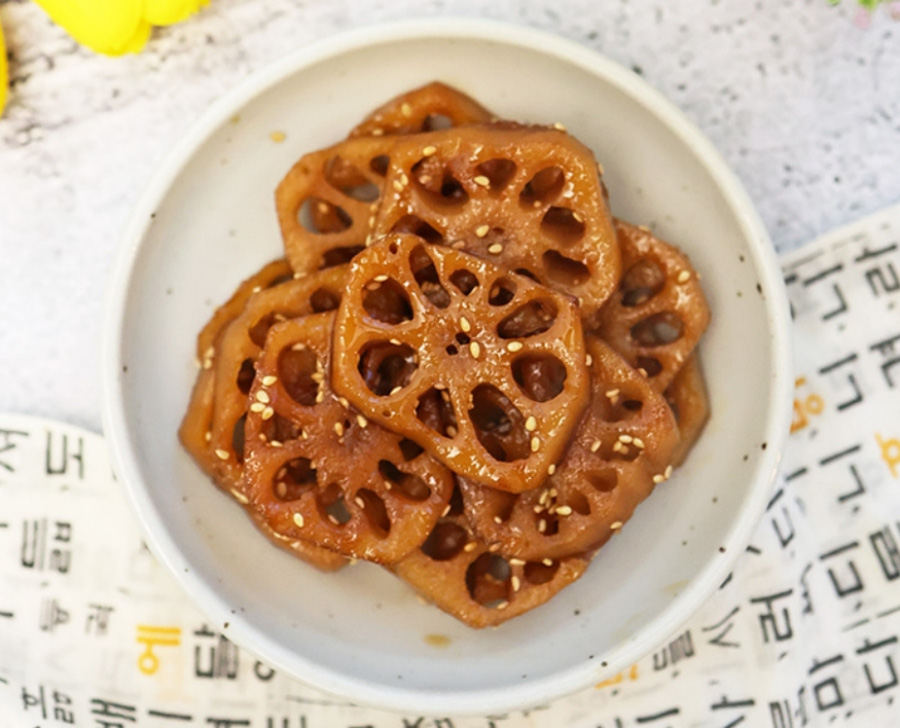 야생에서 채취를 한 연근을 깨끗하게 세척을 한 후에 편으로 썰어 놓은 것을 간장에 졸여서 만든 연근조림을 하얗고 동그란 그릇에 수북하게 놓아두고 찍은 사진