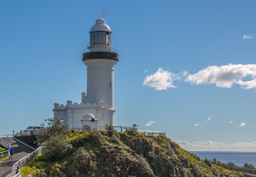 파란 하늘 아래 호주 바이런 베이 절벽 위에 위치한 케이프 바이런 등대의 전경. 왼쪽으로는 등대로 이어지는 산책로가 있고, 오른쪽으로는 끝없는 태평양 수평선이 펼쳐진 모습.