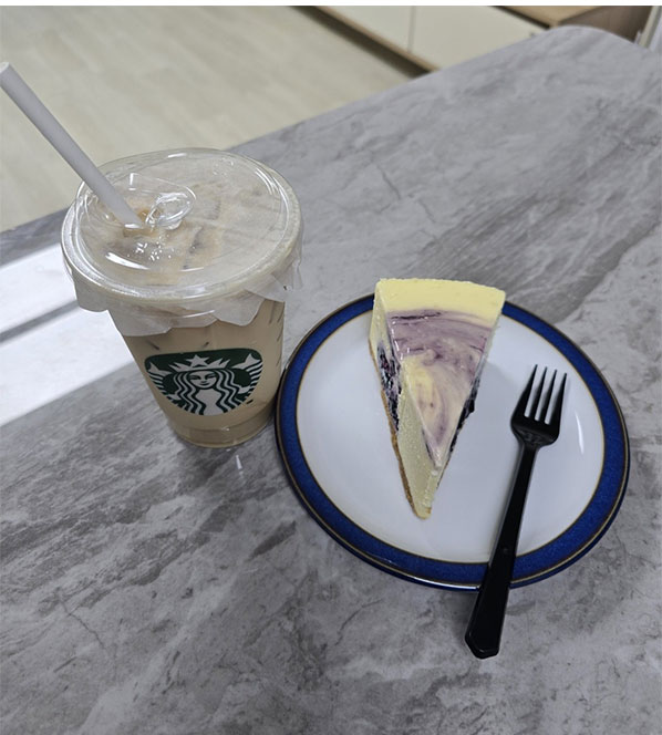 “테이블 위에 놓인 스타벅스 아이스 라떼와 블루베리 치즈케이크, 집에서 카페 분위기를 즐기는 장면.”