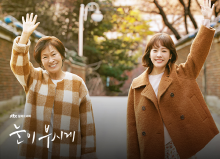 드라마 눈이 부시게의 주인공인 두 여성이 갈색 코트를 입고 골목에서 웃으며 손을 흔드는 모습