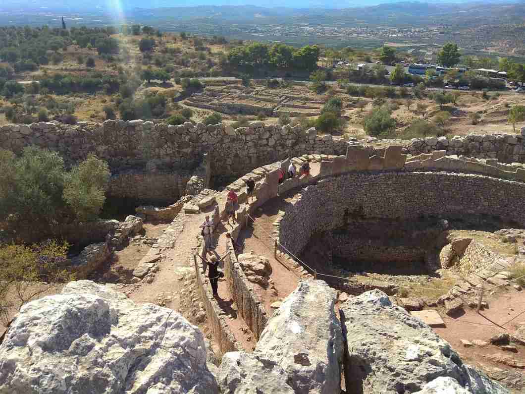 고대 미케네 유적의 원형 무덤지와 성벽, 탐방 중인 방문객들이 보이는 사진입니다.